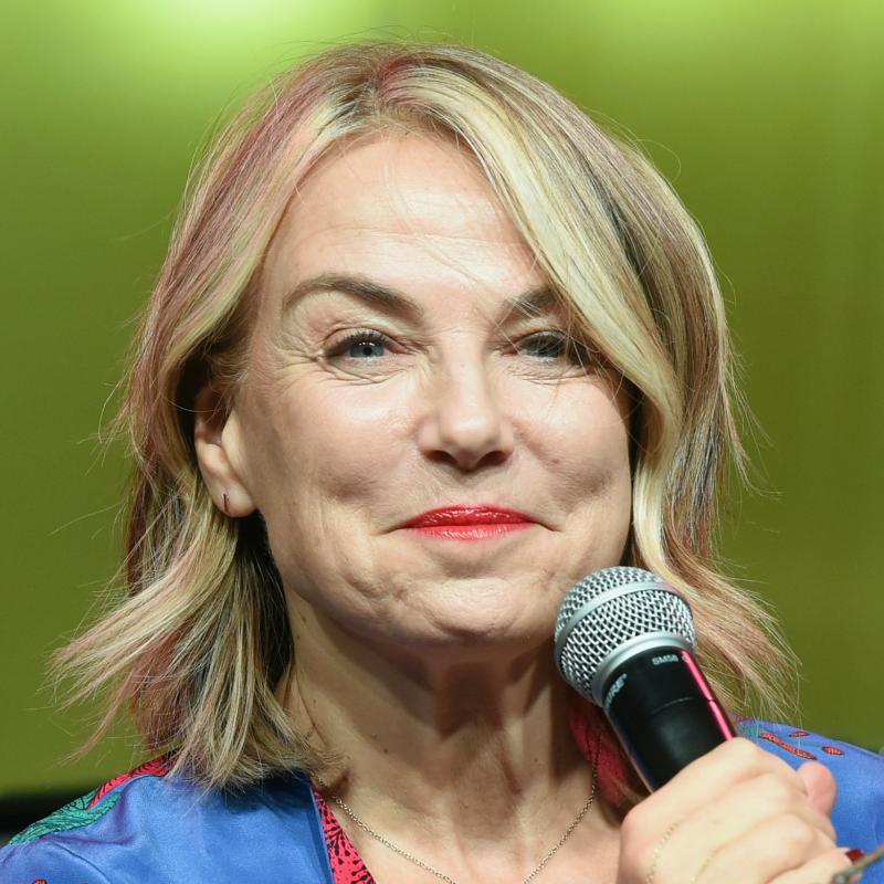 Psychotherapist and podcast host Esther Perel smirks while holding a microphone